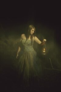 girl in the dark with a lamp, in a long dress, with long hair.